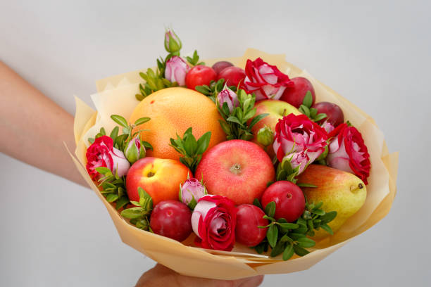 Unique festive bouquet consisting of apples, pears, plums, grapefruits and blooming roses in the hands of a girl stock photo