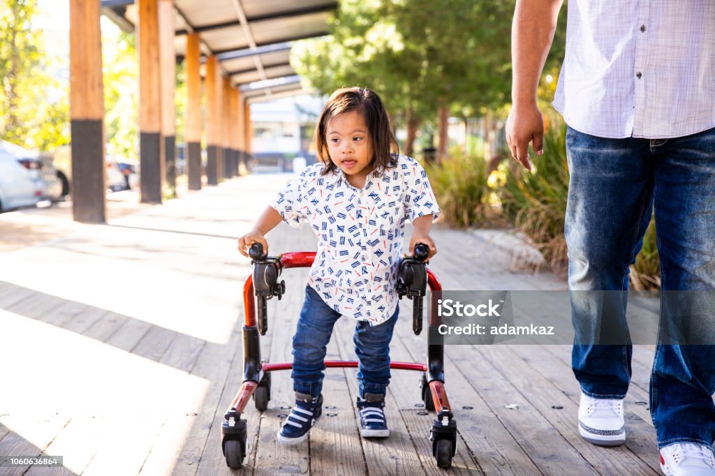 Hispanic Boy with Down's Syndrome Using Walker with Dad A young hispanic boy with down's syndrome walks using a walker with his dad. Child Stock Photo