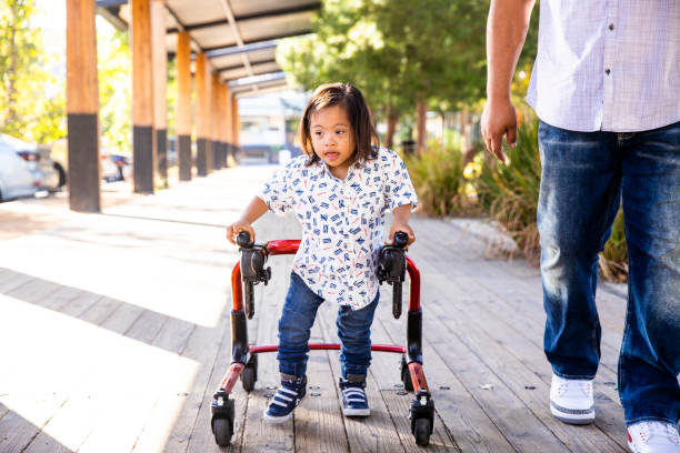 Hispanic Boy with Down's Syndrome Using Walker with Dad A young hispanic boy with down's syndrome walks using a walker with his dad. mobility walker stock pictures, royalty-free photos & images