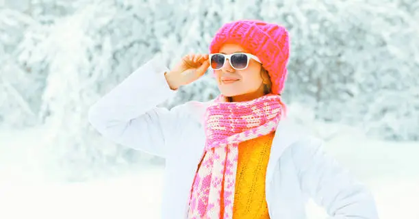 Stylish young woman wearing a colorful knitted hat scarf over snowy background