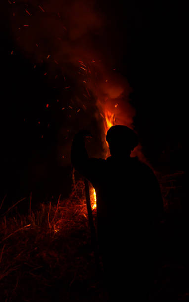 istock Man with stick silhouette burning dry grass at night 1060648930