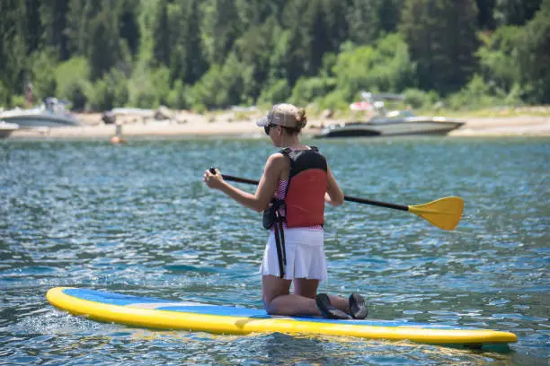 Active fit woman (30s) kneels on a stand up paddleboard on Lake Tahoe in the summer.