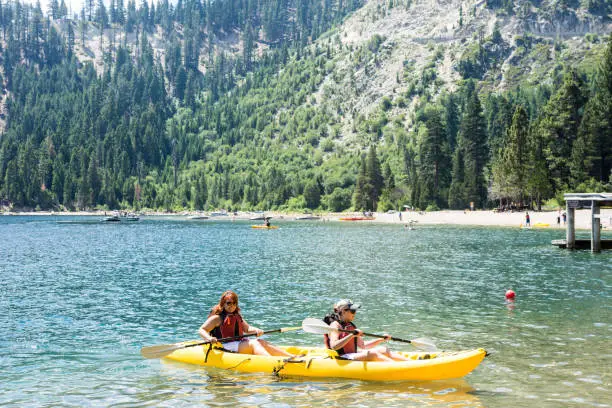 Two female friends row in a dual kayak on Lake Tahoe in Emerald Bay. Concept for teamwork, female friendship, working together