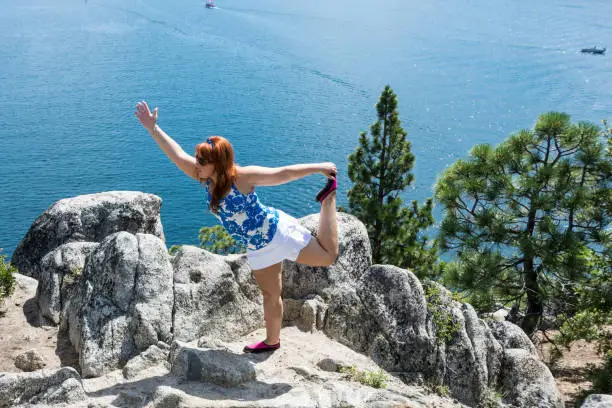 Red head hair ginger woman does a yoga mediation pose on a rock on Fannette Island in Lake Tahoe California