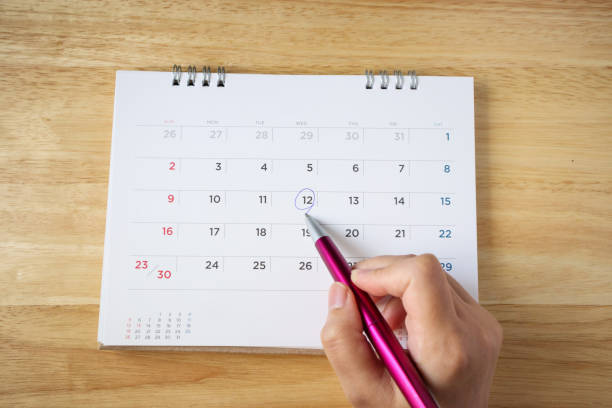 istock calendar page on table with female hand holding pen, top view 1060667294
