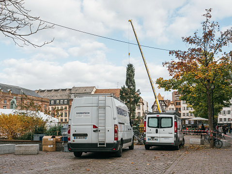 Strasbourg: SWhite vans in Strasbourg Christmas Tree Install in central Place Kleber Square by gigantic crane for the upcoming winter holidays