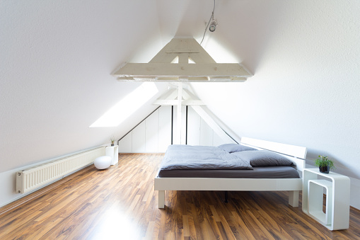 Wide angle view of modern, bright, puristic attic bedroom with double bed and gray bedclothes