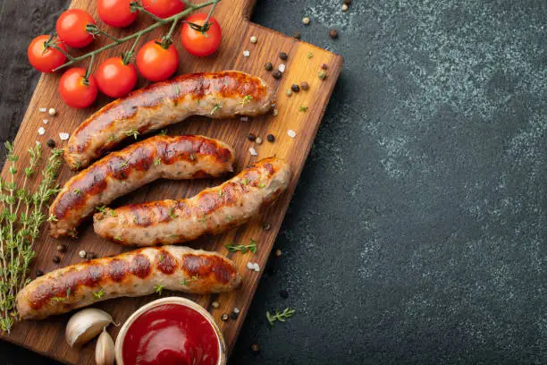 Photo of Fried sausages with sauces and herbs on a wooden serving Board. Great beer snack on a dark background. Top view with copy space