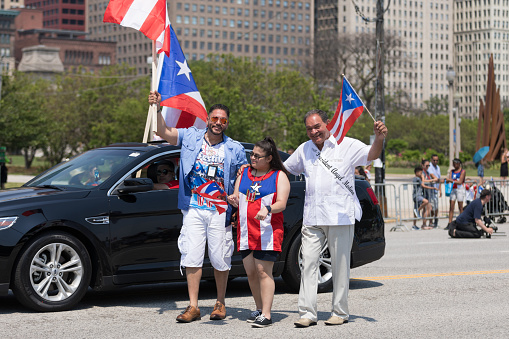 Chicago, Illinois, USA - June 16, 2018: The Puerto Rican Day Parade, Two puerto rican men and a woman pose for the camera holding puerto rican flags