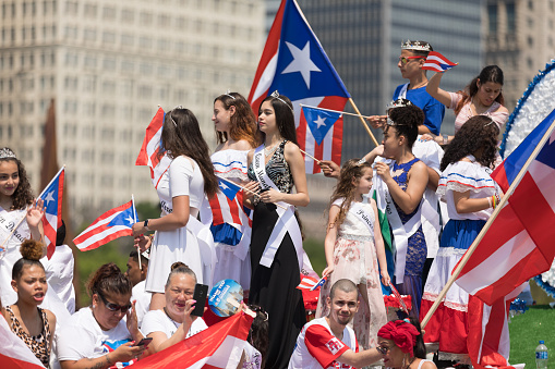 Chicago, Illinois, USA - June 16, 2018: The Puerto Rican Day Parade, Puerto rican beauty queens on a float waving puerto rican flags, going down the street