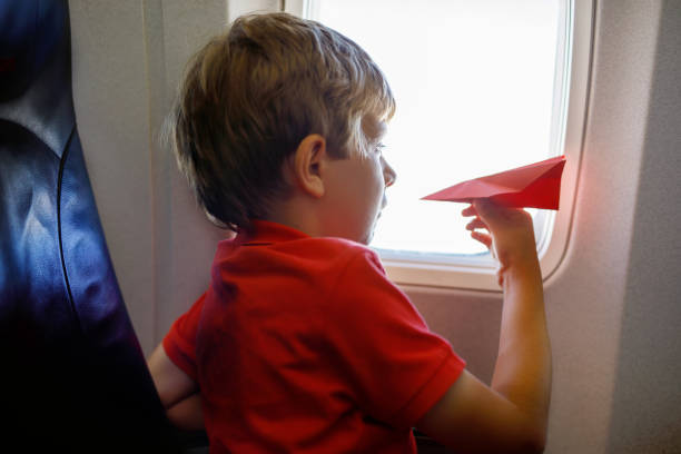 istock Little kid boy playing with red paper plane during flight on airplane 1060742610