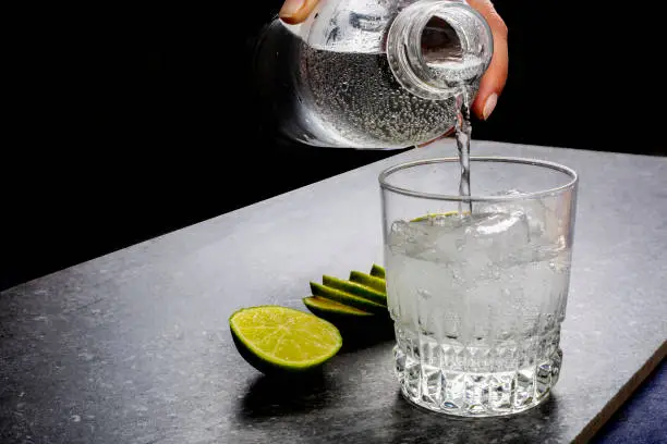 Water being poured into a glass next to sliced lime
