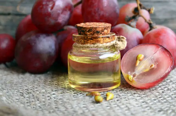 Bottle of organic grape seed oil for spa and bodycare and fresh ripe grapes berries on old wooden table.Healthy food,Bio,Eco products concept.Selective focus.