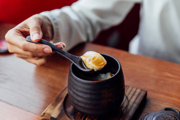 istock Japanese Caramel Pudding served in black ceramic cup that scoop soft pudding by woman hand. 1060744838