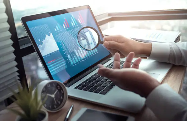 Business concepts with businessman holding magnifying glass with graph chart on computer laptop.For investment analysis,research market ideas