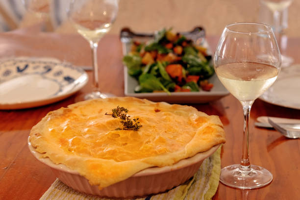 Savory chicken pie with wine glasses and a dish of salad on a wooden table ready for eating
