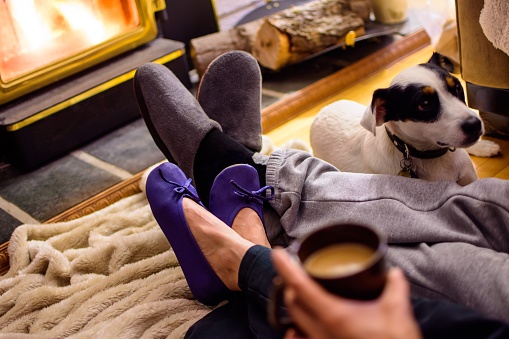 Couple relaxing with legs crossed wearing slippers together near fireplace with cute little dog drinking coffee cozy at home on winter night family moments