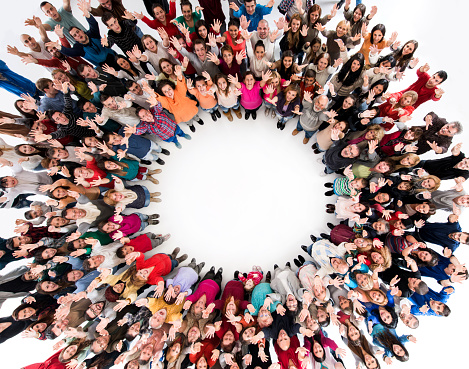 Directly above view of large group of happy people standing in circle with their arms raised. They are looking at camera.