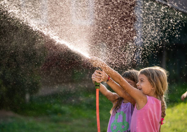 istock Two girls having fun while splashing water with garden hose in the backyard.. 1060762610