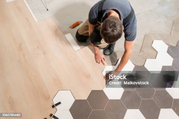 Male Worker Installing New Wooden Laminate Flooring The Combination Of Wood Panels Of Laminate And Ceramic Tiles In The Form Of Honeycomb Kitchen Renovation Stock Photo - Download Image Now