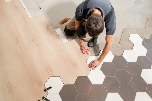 Photo of Male worker installing new wooden laminate flooring. The combination of wood panels of laminate and ceramic tiles in the form of honeycomb. Kitchen renovation.