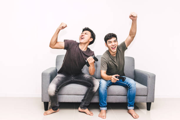 Two friends sitting on sofa and enjoying play video game together at home stock photo