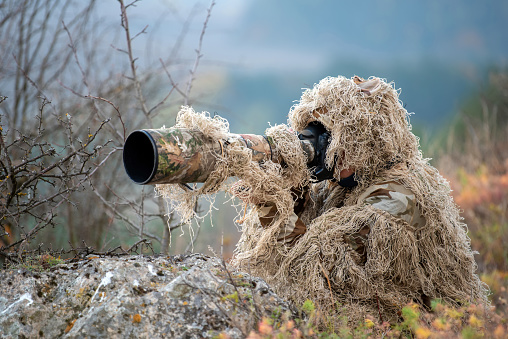 Camouflage wildlife photographer in the ghillie suit working in the wild
