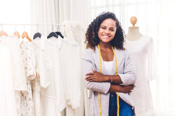 Smiling african american black woman fashion designer with arms crossed standing near mannequin and clothes at workshop studio stock photo