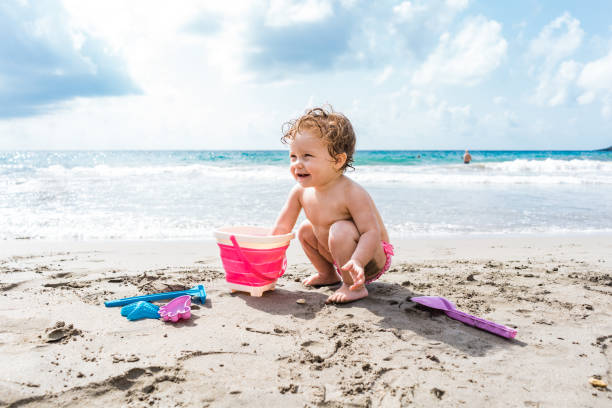 Baby playing on sandy beach with bucket and spade Toddler at the seaside playing on sandy beach with bucket and spade baby squatting stock pictures, royalty-free photos & images
