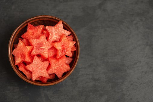Watermelon slices in the shape of a star in bowl on a black plate. Top view, with copy space.