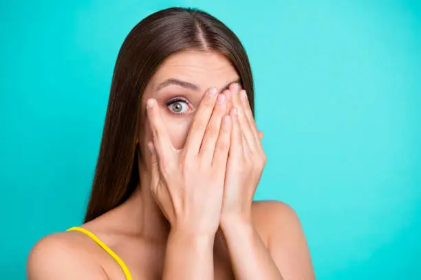 Photo of Close-up portrait of nice funny shocked attractive straight-haired girl, covering face with palms, one eye peeping, isolated on green turquoise background