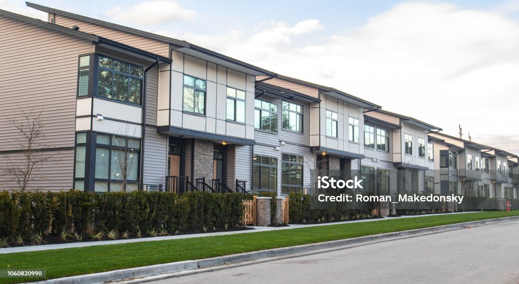 A street of family houses in suburban area with concrete side walk and asphalt road in front. Residential houses with cars parked on driveways in front. House Stock Photo