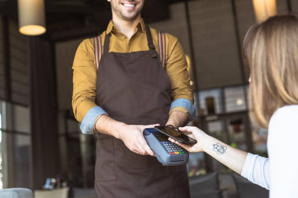 istock cropped shot of smiling waiter holding payment terminal while customer doing contactless purchase with smartphone in cafe 1060823084