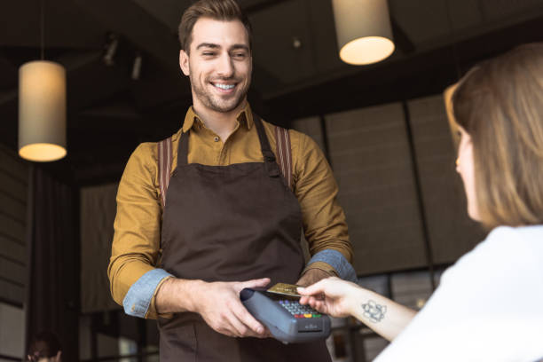istock smiling young waiter holding payment terminal while customer doing contactless purchase with credit card in cafe 1060823102