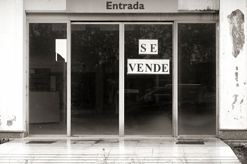 Detail of the entrance door of an empty property needing repairs. For sale sign in spanish language. Black and white image.