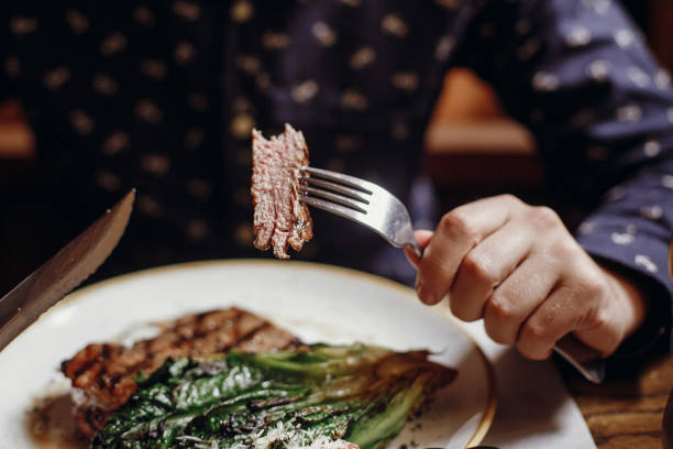 포크와 나이프를 들고와 카페 거리에서 테이블에 구운된 양배추, 토마토와 치즈 맛 있는 육즙이 스테이크를 먹는 손. 바베 큐 식당에서 야채와 함께 시음 하는 남자 - close up green plate salad 뉴스 사진 이미지