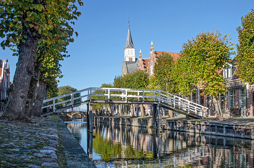 Sloten, The Netherlands, October 28, 2018: view along the lenght of the tree-lined main canal in autumn towards a white wooden bridge and the tower of the church