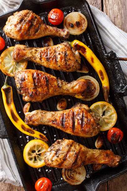 istock Delicious food: grilled chicken drumstick legs with vegetables in a grill pan close-up on a table. Vertical top view, rustic 1060858440