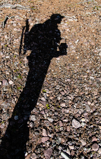 shadow of a man with a camera and a backpack with a tripod outside and a cap on