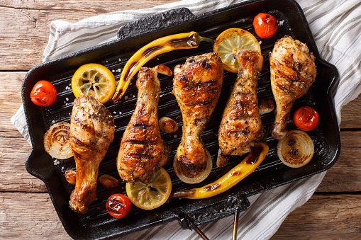 Home barbecue grilled chicken drumstick legs with vegetables in a frying pan grill closeup on a table. horizontal top view from above