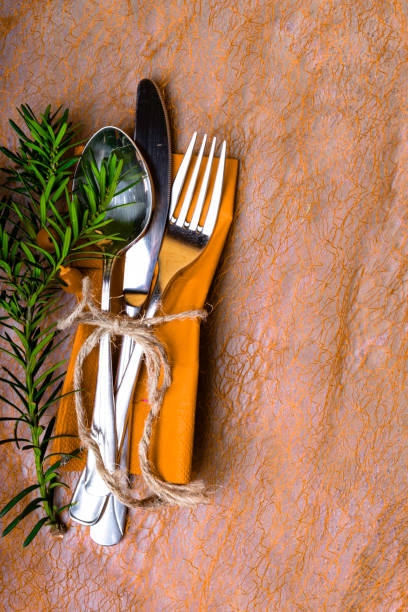 Christmas and New Year table setting. Holiday decoration, spoon, fork, knife on napkin, with rope, cones, Christmas tree branch on orange table, copy space