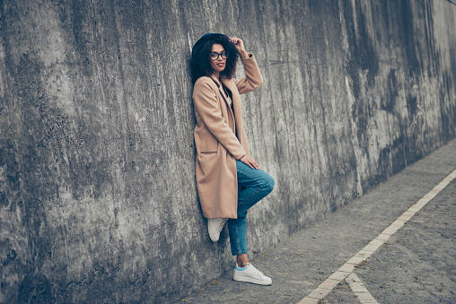 Full length body size profile side view portrait of nice cheeky confident gorgeous attractive curly-haired lady in cozy beige season look topcoat eyeglasses eyewear outdoor touching hat