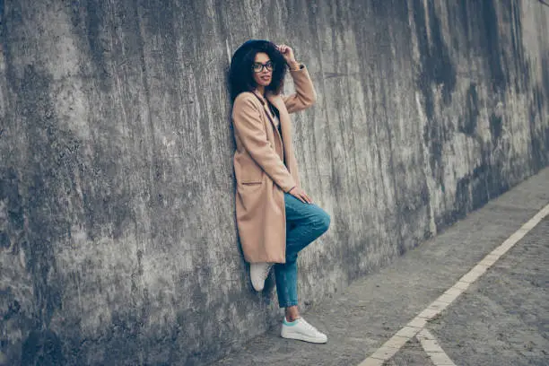 Photo of Full length body size profile side view portrait of nice cheeky confident gorgeous attractive curly-haired lady in cozy beige season look topcoat eyeglasses eyewear outdoor touching hat