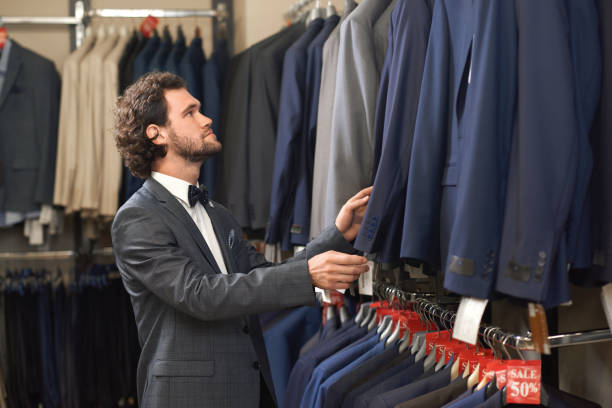 istock Young handsome man in costume looking for jacket in shop. 1060879786