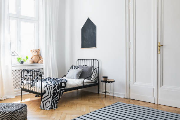 Black poster above bed with patterned sheets in white bedroom interior with plush toy. Real photo