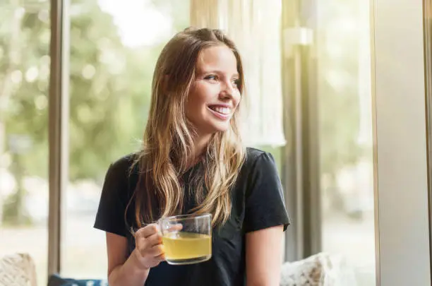 Beautiful young woman at coffee shop holding a green tea cup looking away and smiling. Female having green tea at coffee shop.