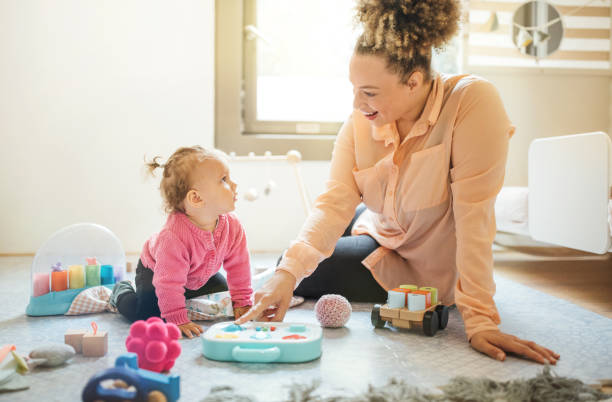 Beautiful young woman with her cute little daughter playing toys. Happy mother and little girl playing together indoors.
