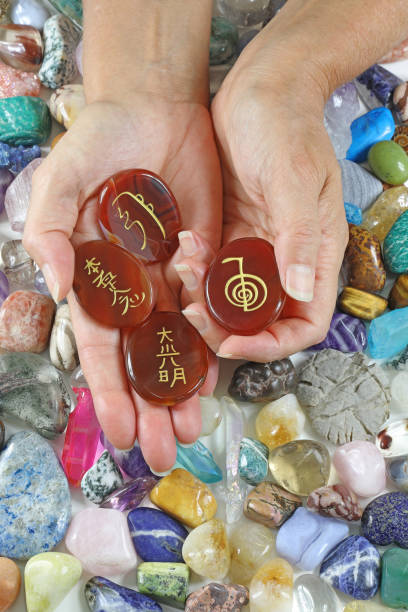 Reiki Healer offering set of Carnelian Palm Stones etched with Reiki symbols against a background of random tumbled crystal stones Carved Carnelian stock pictures, royalty-free photos & images