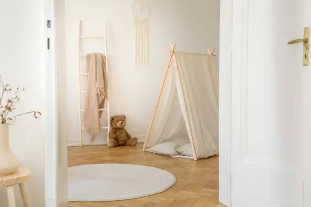 Photo of Stylish kids playroom with white tent, teddy bear, macrame on the wall and round carpet on the parquet, real photo with copy space