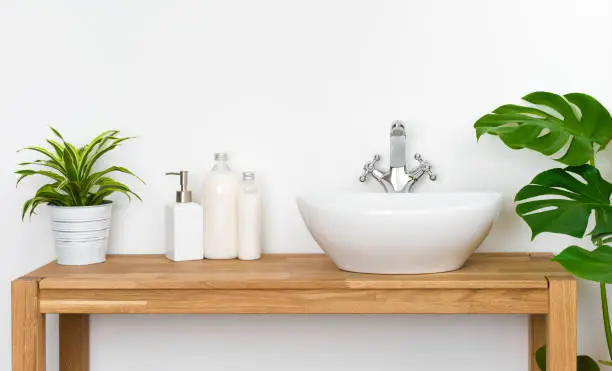 Bathroom wooden table with washbasin, faucet, plants and soap bottles